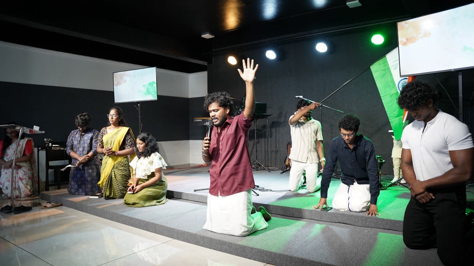 Young people kneeling in prayer on stage in front of an Indian flag